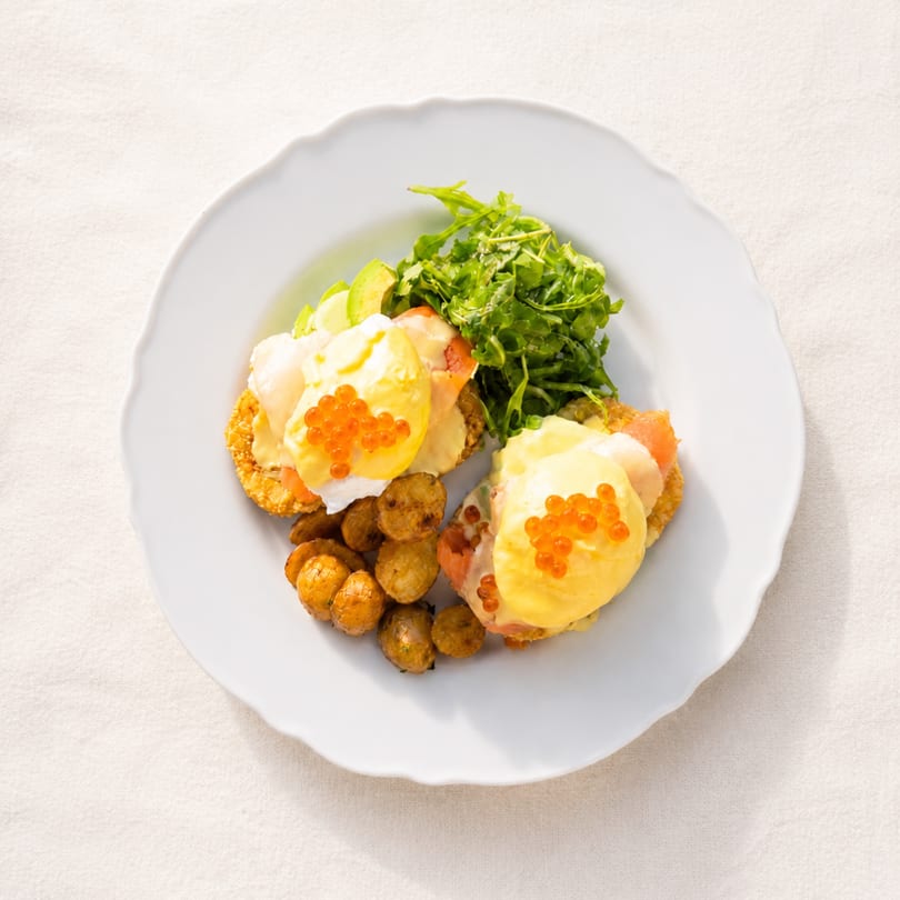 Eggs Benedict with salmon, avocado, caviar, roasted potatoes, and arugula on a white plate.